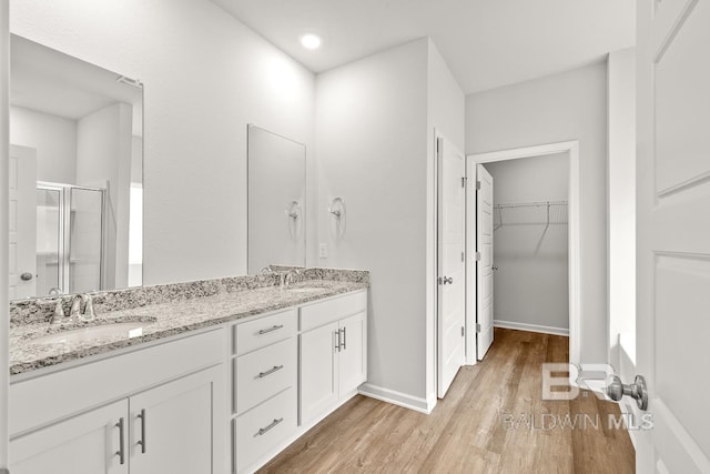 full bathroom featuring a stall shower, a sink, a spacious closet, and wood finished floors