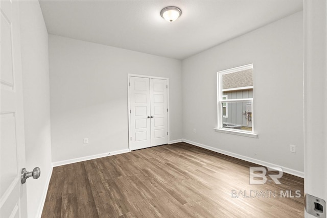 unfurnished bedroom featuring a closet, wood finished floors, and baseboards