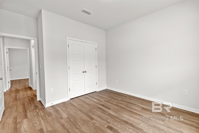 unfurnished bedroom with a closet, wood finished floors, visible vents, and baseboards