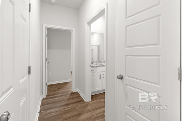 hall with a sink, baseboards, and dark wood-type flooring