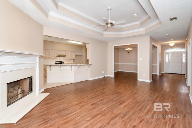 unfurnished living room with ceiling fan with notable chandelier, ornamental molding, visible vents, a fireplace, and a tray ceiling