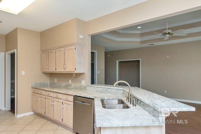 kitchen featuring a tray ceiling, stainless steel dishwasher, light brown cabinets, and a sink