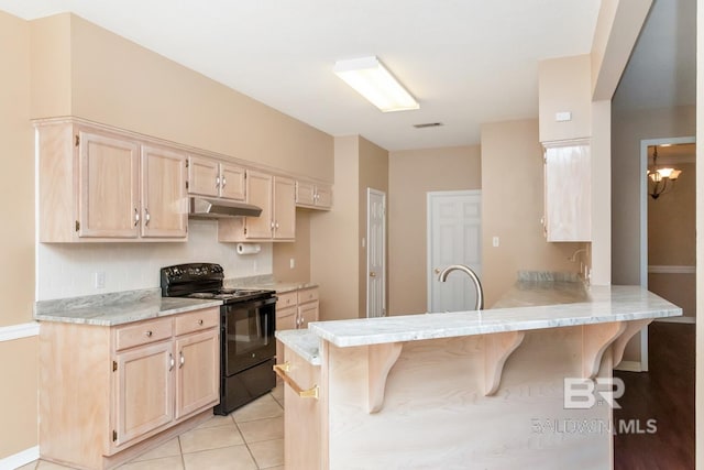 kitchen featuring light brown cabinetry, under cabinet range hood, black / electric stove, a peninsula, and a kitchen breakfast bar