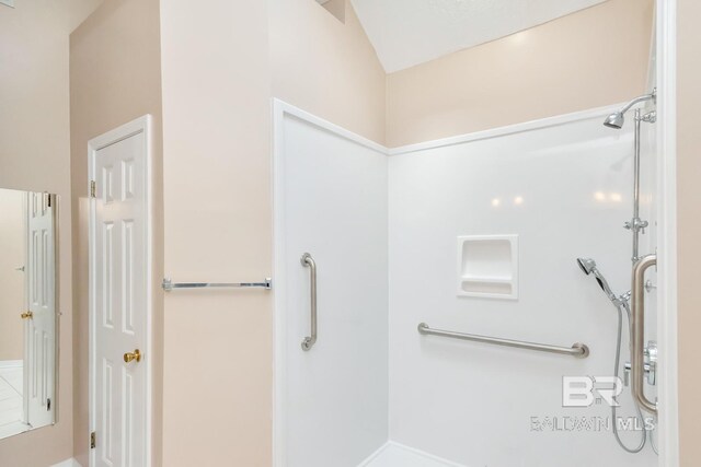 bathroom featuring a shower, baseboards, and vaulted ceiling