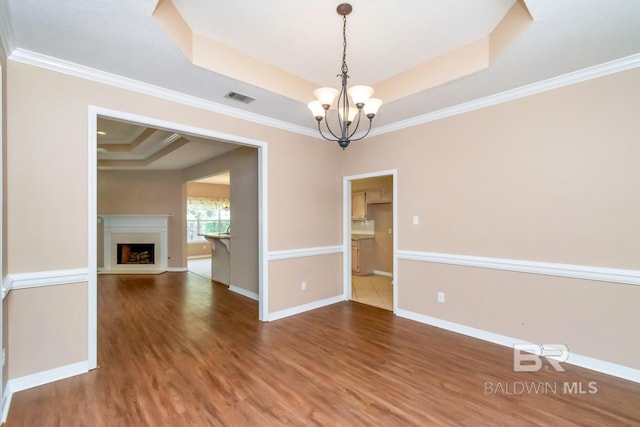 unfurnished dining area with a notable chandelier, baseboards, visible vents, wood finished floors, and a raised ceiling
