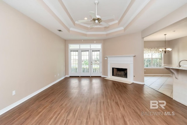 unfurnished living room with ceiling fan with notable chandelier, crown molding, visible vents, a raised ceiling, and a fireplace with raised hearth