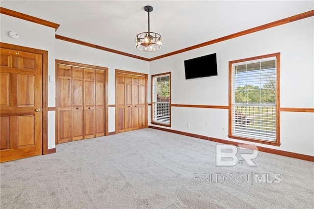 unfurnished bedroom featuring crown molding, carpet, two closets, and an inviting chandelier