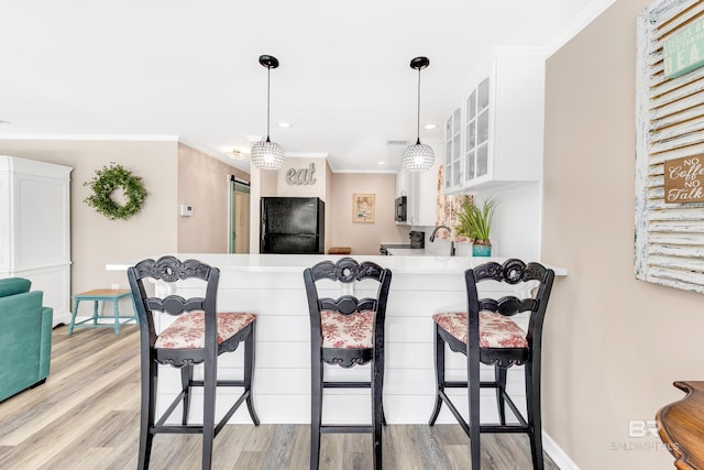 kitchen with kitchen peninsula, appliances with stainless steel finishes, pendant lighting, white cabinets, and light hardwood / wood-style floors