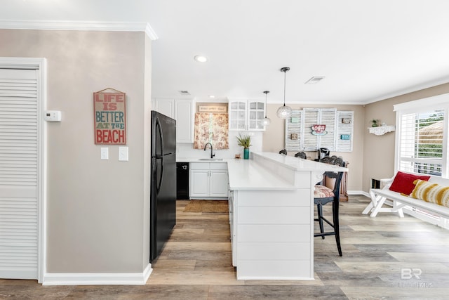 kitchen with kitchen peninsula, pendant lighting, a kitchen bar, white cabinets, and black appliances