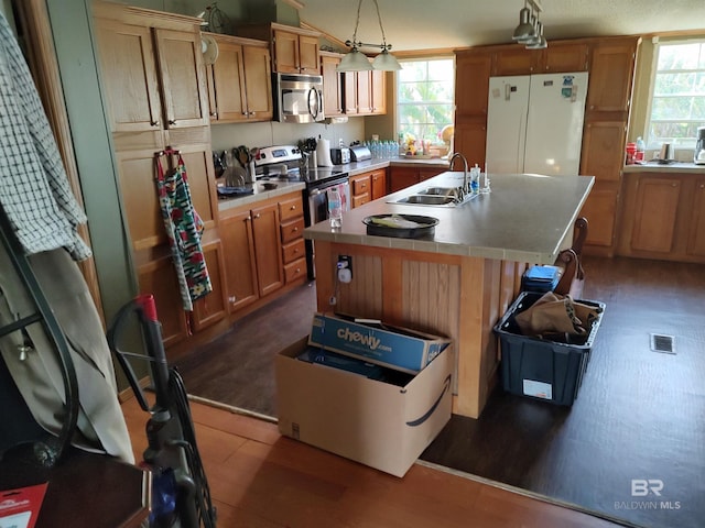 kitchen with stainless steel appliances, a healthy amount of sunlight, sink, decorative light fixtures, and a center island with sink