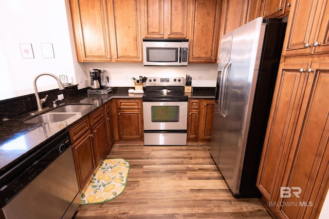 kitchen featuring light hardwood / wood-style floors, stainless steel appliances, sink, and dark stone counters