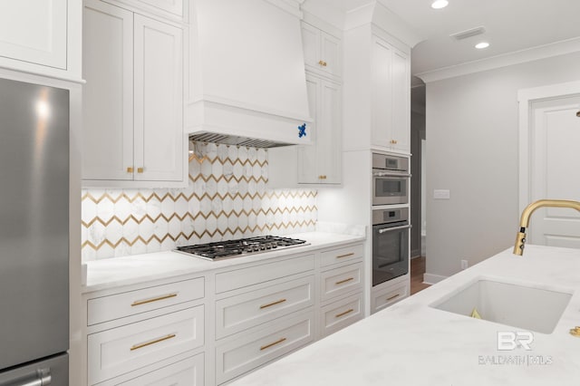 kitchen featuring tasteful backsplash, premium range hood, stainless steel appliances, sink, and white cabinetry