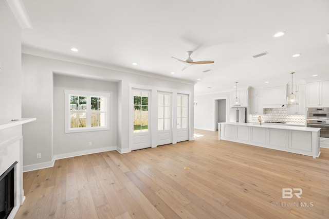 unfurnished living room with ceiling fan, crown molding, and light hardwood / wood-style flooring