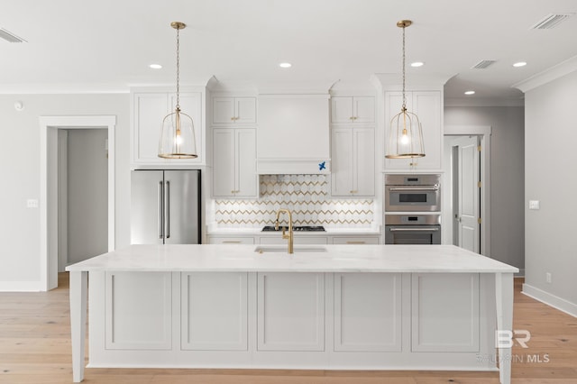 kitchen featuring backsplash, premium range hood, a kitchen island with sink, white cabinets, and appliances with stainless steel finishes