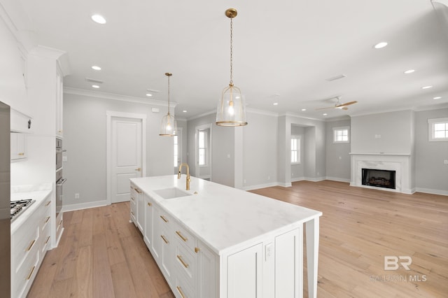 kitchen with a center island with sink, white cabinets, sink, hanging light fixtures, and a premium fireplace