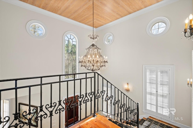 stairway featuring a notable chandelier, wood-type flooring, wood ceiling, and crown molding