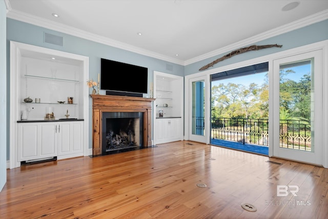 unfurnished living room featuring built in shelves, light hardwood / wood-style floors, and crown molding