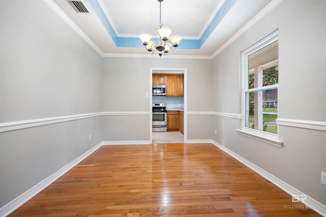 unfurnished room with light wood-type flooring, a raised ceiling, ornamental molding, and an inviting chandelier