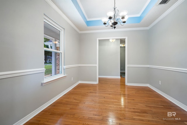 empty room with wood-type flooring, a tray ceiling, crown molding, and a chandelier