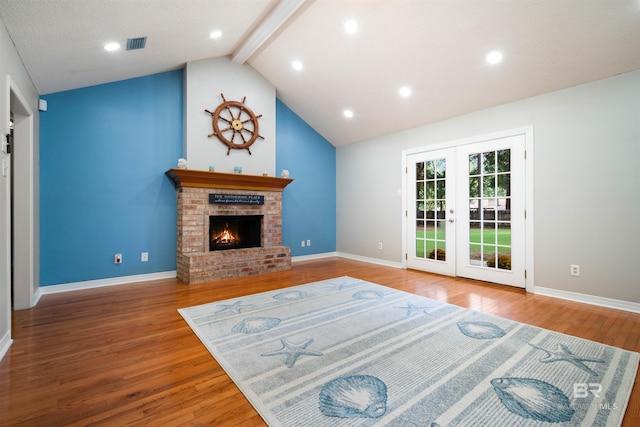 living room with a brick fireplace, wood-type flooring, vaulted ceiling with beams, and french doors