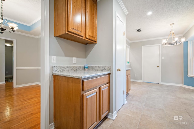 kitchen featuring pendant lighting, light wood-type flooring, a chandelier, a textured ceiling, and ornamental molding