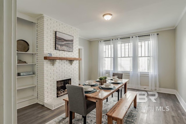 dining room with hardwood / wood-style flooring, a fireplace, crown molding, and brick wall