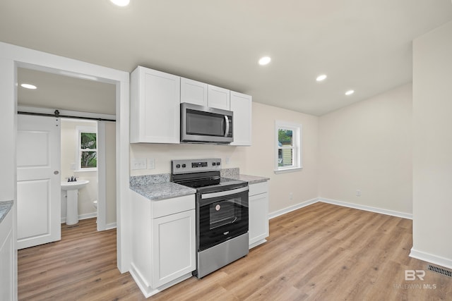 1096 S Pine St, Loxley, AL 36551 - kitchen with appliances with stainless steel finishes, white cabinets, light wood finished floors, a barn door, and healthy amount of natural light