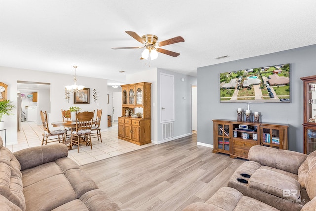 living room featuring washer / dryer, light hardwood / wood-style flooring, a textured ceiling, and ceiling fan with notable chandelier