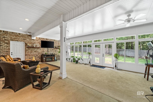 living room featuring french doors, a wood stove, ceiling fan, brick wall, and decorative columns