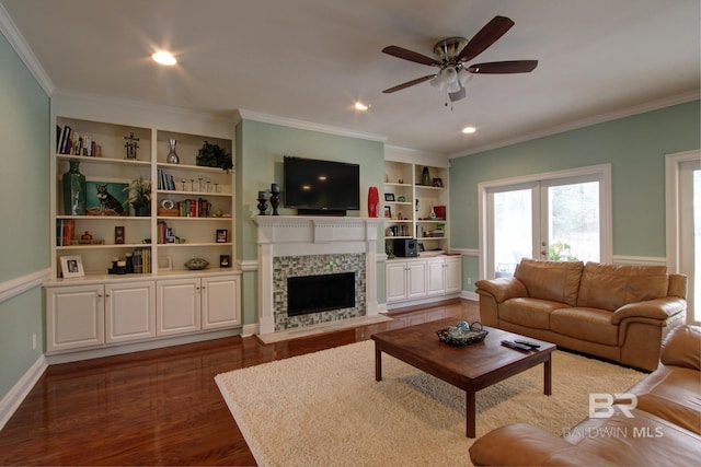 living room with built in features, a ceiling fan, dark wood-style floors, a fireplace with flush hearth, and ornamental molding