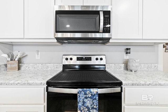 kitchen with stainless steel appliances, white cabinetry, and light stone counters