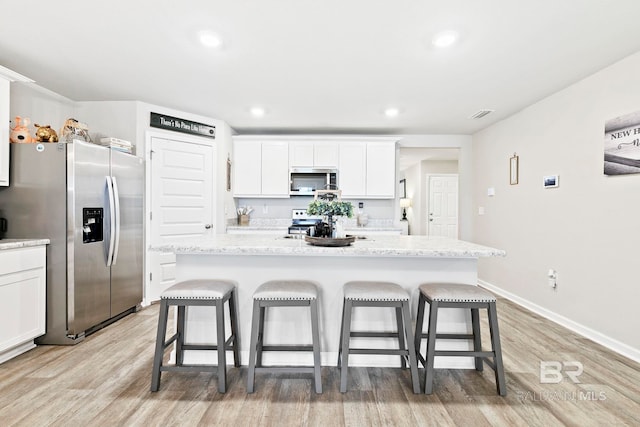 kitchen featuring a kitchen island, a kitchen bar, white cabinetry, and appliances with stainless steel finishes