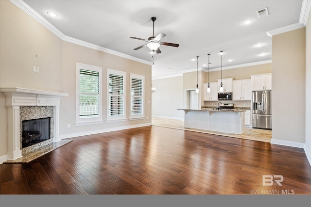 unfurnished living room with a high end fireplace, ornamental molding, wood-type flooring, and ceiling fan