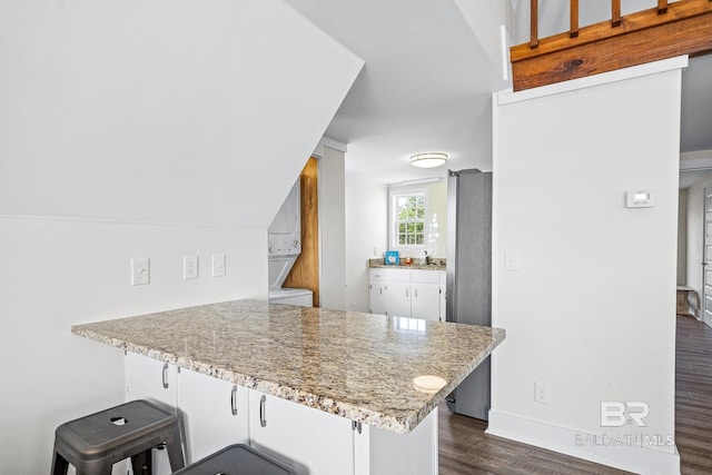 kitchen featuring stainless steel fridge, white cabinetry, stacked washer and clothes dryer, light stone counters, and kitchen peninsula