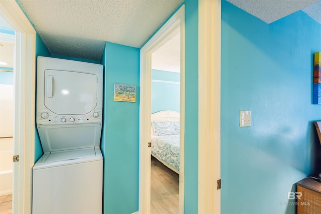 washroom featuring a textured ceiling, light hardwood / wood-style floors, and stacked washer and dryer