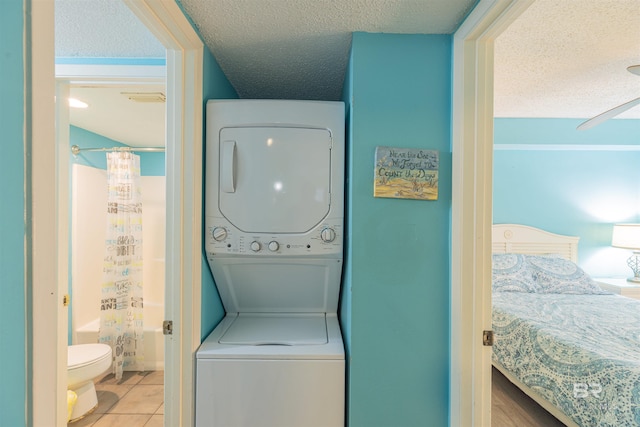 clothes washing area with light tile patterned flooring, stacked washer and clothes dryer, and a textured ceiling