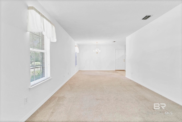 carpeted empty room featuring baseboards, a chandelier, and visible vents