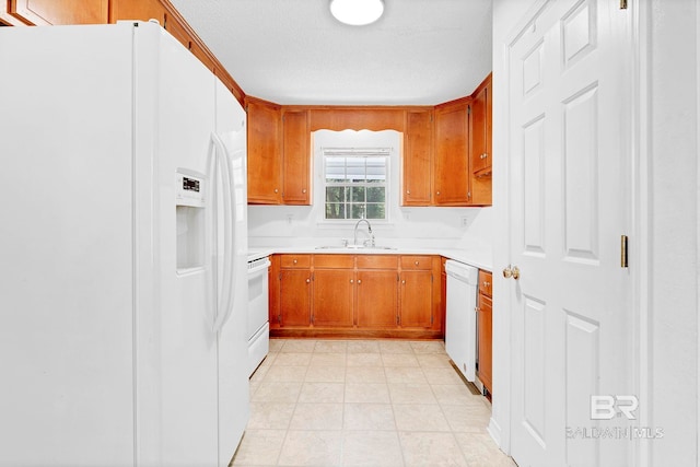 kitchen with a sink, white appliances, light countertops, and brown cabinets