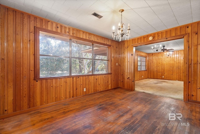 spare room with an inviting chandelier, wood-type flooring, and wood walls