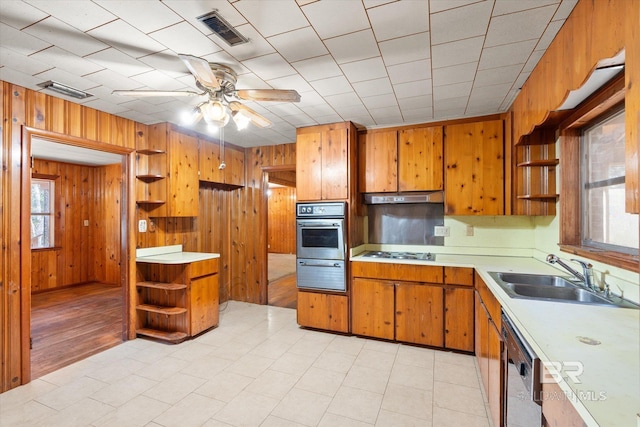 kitchen with sink, wood walls, stainless steel oven, gas cooktop, and dishwashing machine