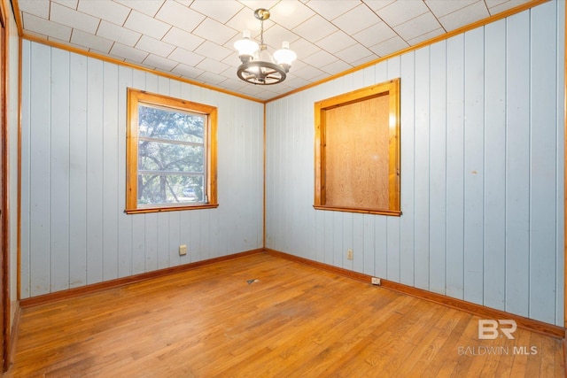 empty room featuring an inviting chandelier, ornamental molding, and wood-type flooring