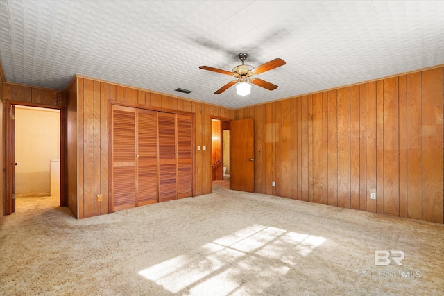 unfurnished bedroom with ceiling fan, wooden walls, carpet floors, and a closet