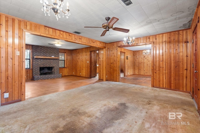 unfurnished living room with ceiling fan with notable chandelier, wooden walls, light carpet, and a fireplace