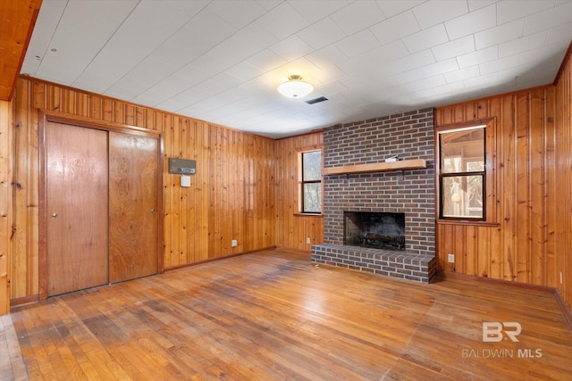 unfurnished living room with a brick fireplace, hardwood / wood-style floors, and wood walls