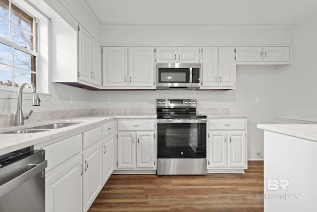 kitchen featuring appliances with stainless steel finishes, sink, white cabinets, hardwood / wood-style flooring, and ornamental molding