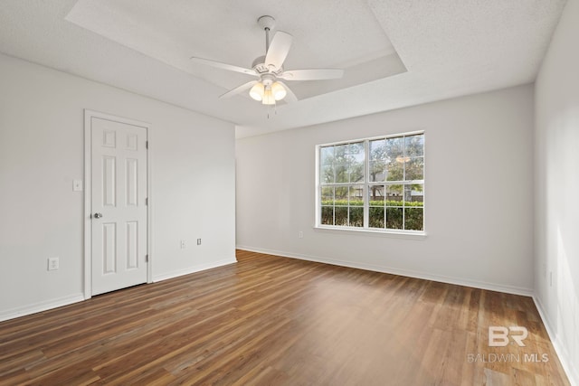 unfurnished room featuring ceiling fan, a tray ceiling, dark hardwood / wood-style flooring, and a textured ceiling