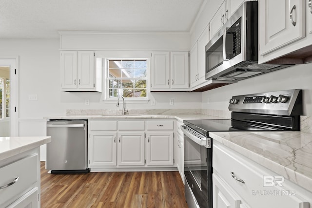 kitchen with sink, appliances with stainless steel finishes, white cabinetry, dark hardwood / wood-style floors, and light stone counters