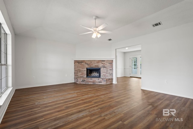 unfurnished living room featuring a brick fireplace, a textured ceiling, dark hardwood / wood-style floors, and ceiling fan