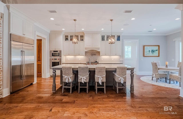 kitchen with appliances with stainless steel finishes, pendant lighting, hardwood / wood-style flooring, ornamental molding, and a center island with sink