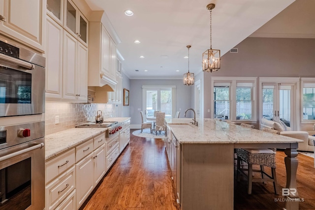 kitchen featuring pendant lighting, tasteful backsplash, a kitchen bar, a kitchen island with sink, and light stone counters